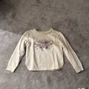 Vit långärmad tröja med tryck från Zadig & Voltaire - Säljer en vit långärmad tröja från Zadig & Voltaire med coolt tryck framtill i rosa, blått och beige. Tröjan har rund halsringning och mjukt bomullsmaterial. Perfekt för dig som gillar unika prints och streetstyle.