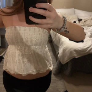 Vit glittrig tubtopp - Säljer en söt vit tubtopp med glittriga detaljer. Toppen har en lätt volang nedtill och är perfekt för dig som vill ha något festligt och trendigt. Passar snyggt till både jeans och kjol. Från Gina Young i storlek 146/152 men funkar bra på mig som vanligtvis har storlek S