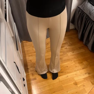 Beiga bootcut-byxor från NA-KD - Snygga beiga bootcut-byxor från NA-KD med markerade sömmar framtill. Byxorna har hög midja och är tillverkade i ett mjukt, stretchigt material som sitter bekvämt. Perfekta för en trendig och stilren look. Storlek M men passar även mig som vanligtvis bär Xs-S, de sitter dock lite lösare.