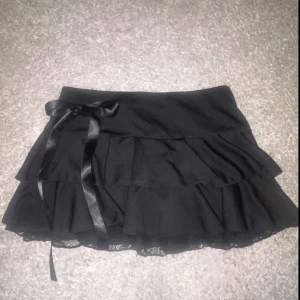 Svart volangkjol med rosett - Supersöt svart kortkjol med dubbla volanger och en sidenrosett i midjan. Kjolen har spetsdetalj längst ner. Köpt här på Plick men säljer pågrund av att den är för kort för mig, skriv gärna om du har frågor!🎀