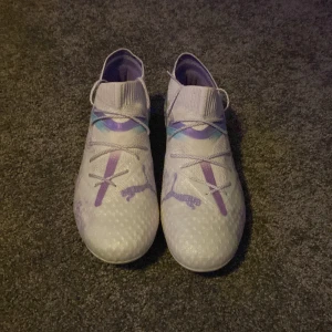 Ljuslila fotbollsskor från Puma - Säljer ett par snygga ljuslila fotbollsskor från Puma med stickad strumpliknande krage och lila detaljer. Skorna har snörning och mönstrad ovandel i syntetmaterial. Perfekta för dig som vill sticka ut på planen!