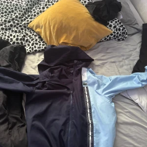 Blå och ljusblå vindjacka från Lacoste - Jackan är perfekt till sommaren när det blåser och rengnar den funkar allmänt under hela sommaren den är som en tunnare hoodie. Köpte den för 1500 på Lacoste.