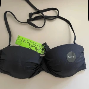 Svart push up bikiniöverdel från Lindex - Svart push up bikiniöverdel från Lindex med avtagbara axelband och knäppning bak. Perfekt för stranden eller poolen, med vadderade kupor för extra lyft. Snygg och enkel design.