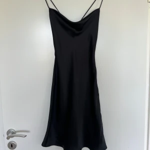 Satinklänning NAKD - Säljer en svart elegant satinklänning med tunna axelband och snygg draperad urringning. Klänningen har öppen rygg med snörning. Superfin till många tillfällen. Väldigt fint skick!