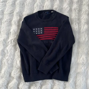 Gant tröja - Mörkblå tröja med amerikansk flagga i rött, vitt och blått på bröstet. Rund halsringning och ribbade muddar vid ärmslut och nederkant. Passar barn i åldern 11-12 år sitter som xxs, lappen har släppt lite men inget stort