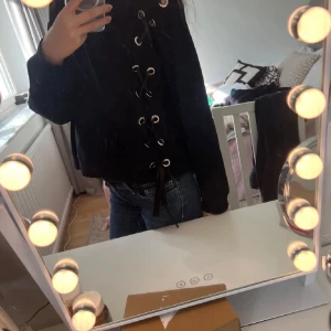 Svart croppad tröja med snörning - Säljer en svart croppad tröja med cool snörningsdetalj längs ena sidan. Tröjan har långa ärmar och rund halsringning. Perfekt för dig som vill ha en trendig och bekväm look.