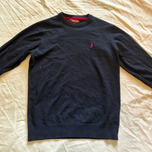 Mörkblå stickad tröja från MCS - Mörkblå stickad tröja från MCS med rund halsringning och röd broderad logga på bröstet. Nyskick, skriv för funderinga 