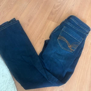 Blå bootcut jeans lågmidjade tryck på fickor  - Säljer ett par  blå bootcut jeans med snygga tryck kontrastsömmar på bakfickorna. Jeansen har normal passform och är tillverkade i ett robust denimtyg. Lågmidjade med utsvängda ben. Lite Mörkare i verkligeheten än på bilderna ,säljs inte längre