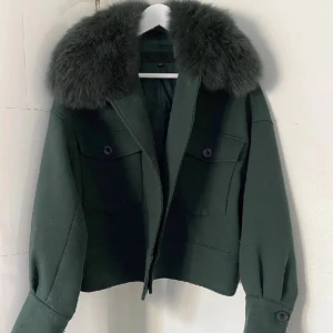 Mörkgrön jacka med pälskrage - Säljer en mörkgrön jacka med stor, fluffig pälskrage. Jackan är croppad och har knappar framtill samt fickor med lock. Perfekt för dig som vill ha en trendig och snygg look. Meotine liknande jacka 