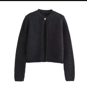 Svart stickad kofta med knapp - En svart/grå stickad kofta från Zara  med rund halsringning och en dekorativ knapp upptill. Koftan har lång ärm och en rak, något croppad passform. Perfekt att slänga över en topp för en enkel men stilren look.(liten i storleken )