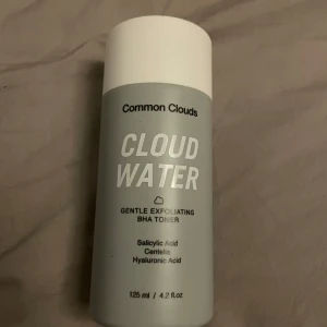 Cloud Water Gentle Exfoliating BHA Toner från Common Clouds - Cloud Water är en mild exfolierande toner med BHA, salicylsyra, centella och hyaluronsyra. Perfekt för att rengöra porer och lugna huden. Flaskan rymmer 125 ml och har en stilren grå och vit design. Oanvänd 