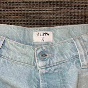 Ljusblå wide leg jeans från Filippa K - Säljer ett par ljusblå jeans från Filippa K i modellen Trucker Jean. Jeansen har raka vida ben och knäppning med knappar passar perfekt för en avslappnad stil.