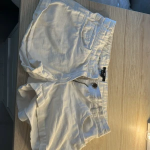 Vita shorts i manchester - Säljer ett par vita shorts i mjuk manchester med normal passform. Shortsen har två  bakfickor, knapp och dragkedja framtill samt bälteshällor. Perfekta för varma dagar och enkel att matcha med olika toppar.