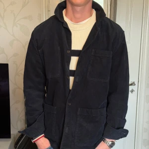 Mörkblå manchester overshirt från East West - Säljer en Mörkblå overshirt i manchester från East West. Jackan har flera stora fickor framtill och stängs med knappar. 