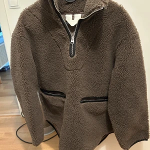 Brun teddyjacka från Arket - Brun teddyjacka med halv dragkedja framtill och två svarta fickor med dragkedja. Lite oversized passform. Den är som ny.