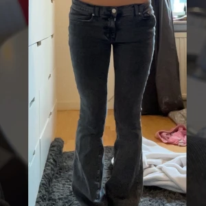 Gråa bootcut jeans - Säljer ett par gråa bootcut jeans med normal passform och klassisk femficksdesign. Jeansen har låg midja och stängs med dragkedja och knapp. Perfekta för dig som gillar en tidlös look med lite utsvängda ben.