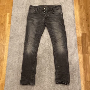 Svarta jeans från Nudie Jeans - Säljer ett par svarta jeans från Nudie Jeans. Klassisk femficksdesign och svarta sömmar på bakfickorna. Jeansen har en slim passform och knappgylf. Nypris: 1800kr. Storlek: W28:L30. Modell: Grim Tim. Skriv vid funderingar