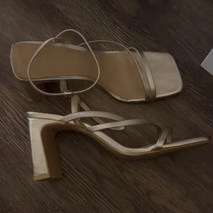Guldiga klackskor - Säljer ett par sandaler i guld med bred klack. Storlek 39. Använd 1-2 gånger❣️Superenkla att gå i, perfekt till balen 👡 