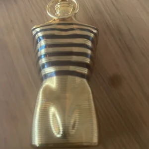 Le Male Le Parfum Eau de Parfum - Säljer en ikonisk herrparfym från Jean Paul Gaultier i en guldig flaska formad som en manlig torso med svarta ränder upptill. Flaskan har en unik design och är perfekt för dig som gillar lyxiga och distinkta dofter.
