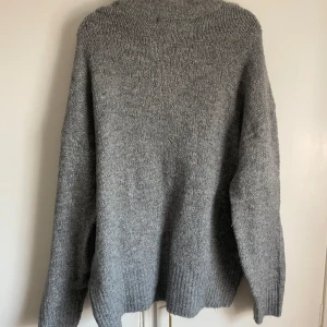 Grå stickad tröja - Mysig grå stickad tröja med lång ärm och ribbade muddar vid ärmslut och nederkant. Perfekt för kyligare dagar och enkel att matcha med olika outfits.