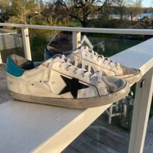 Vita Golden Goose sneakers - Säljer ett par vita sneakers från Golden Goose. Storlek 42EU. De är väl använda med en skada vid hälen vilket syns på bild 4. Självklart äkta. Hör av er vid frågor!