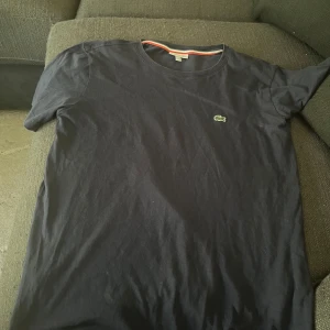 Mörkblå t-shirt  från Lacoste - Mörkblå t-shirt från Lacoste med klassisk rund hals och den ikoniska krokodilloggan broderad på bröstet. T-shirten är enkel och stilren, perfekt till många olika outfits.