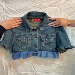 Mörkblå jeans bolero - Mörkblå jeans bolero med volang. Storlek: M. Mått: Plaggets längd: 36 cm. 