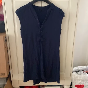 Mörkblå klänning från Vila - En enkel och stilren mörkblå klänning från Vila med korta ärmar och knappar framtill. Perfekt för en avslappnad look och lätt att matcha med accessoarer.