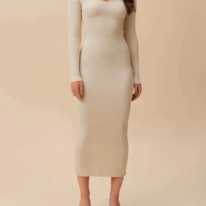 Beige ribbad långklänning - Säljer en beige ribbad långklänning med lång ärm och v-ringad hals. Klänningen har en tight passform och en slits bak för extra rörelsefrihet. Perfekt för dig som gillar stilrena och enkla plagg med en modern touch.
