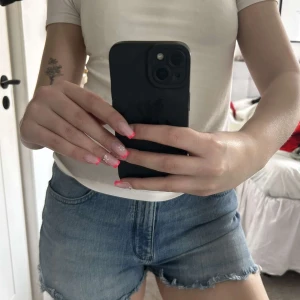 Jeans shorts  -  ett par klassiska blå jeansshorts från Wrangler med råa kanter och femficksmodell. Shortsen har normal passform och är medel missade men skulle kunna vara lågmidjade om man viker ner de. Perfekta för varma dagar och enkel att matcha med olika toppar. Fint skick!