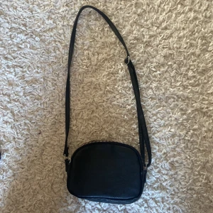 Svart axelväska med dragkedja - Snygg svart axelväska med två separata fack och dragkedjor. Perfekt för att hålla dina saker organiserade. Väskan har en justerbar axelrem för bekväm användning.