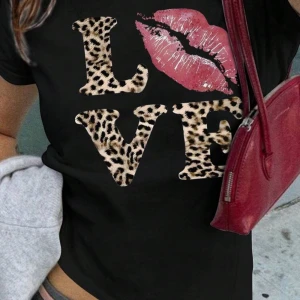 Svart t-shirt med leopardmönster och läpptryck - Cool svart t-shirt med texten 'LOVE' där bokstäverna är i leopardmönster och ett läpptryck i rosa. Perfekt för en trendig look! aldrig använd!!