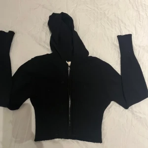 Svart croppad hoodie med dragkedja - Snygg svart croppad hoodie med dragkedja framtill. Perfekt för en avslappnad stil. Den har långa ärmar och en bekväm huva.