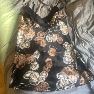 Svart blommig blus med tunna axelband - Snygg svart blus med blommigt mönster i beige och vitt. Blusen har tunna axelband och en elegant passform. Perfekt för en somrig dag eller en kväll ute. 🌸