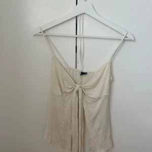 Vitt topp från Gina Tricot - Säljer en stilren vit topp från Gina Tricot med smala axelband och knytdetalj framtill. Toppen har en luftig och lätt design, perfekt för varma dagar. Passar bra till både jeans och kjol. 🌼