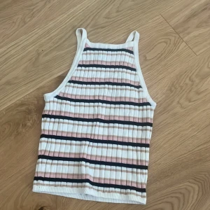Randig ribbad linnetopp från H&M Divided - Säljer en randig ribbad linnetopp från H&M Divided i färgerna vit, rosa, beige och svart. Perfekt för sommardagar med sin ärmlösa design och bekväma passform. Väldigt stretchig