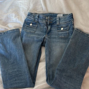Blå jeans med fickdetaljer - Snygga blå jeans med dubbla knappar och dragkedja. De har unika fickdetaljer med knappar framtill och en klassisk jeanslook. Perfekta för en avslappnad stil. Passar storlwk xs och s