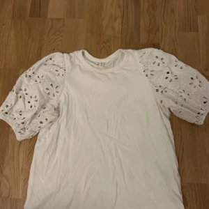 Vit topp med spetsärmar - Säljer en vit topp med vackra spetsärmar i blommigt mönster. Toppen har en rund halsringning och korta ärmar som ger en romantisk touch. Perfekt för sommarens varma dagar.