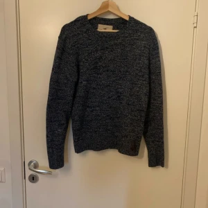 Mörkblå stickad tröja från Hollister - Säljer en mörkblå stickad tröja från Hollister. Tröjan har en klassisk rund hals och långa ärmar, perfekt för kyligare dagar. Den är i en snygg melerad design som ger en stilren look.