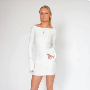 Studentklänning  - Elegant vit klänning med lång ärm och en stilren öppen rygg. Perfekt för studenten eller skolavslurning. Klänningen har en tight passform som framhäver figuren. Helt oanvänd. Nypris 899 kr.