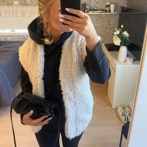 Krämvit pälsväst - Säljer en mysig vit pälsväst perfekt för kyliga dagar. Västen har en normal passning och är utan ärmar, vilket gör den lätt att bära över en hoodie eller tröja. Den är både stilren och funktionell.