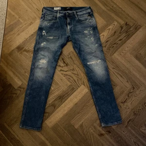 Blå jeans från Replay - Snygga blå jeans från Replay med slitna detaljer och en slim fit passform. Perfekta för en trendig look. De har en klassisk femficksdesign och en knappgylf.