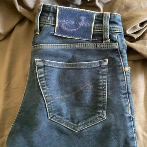 Blå jeans från Jacob Cohen - Snygga blå jeans från Jacob Cohen. Storlek 30 och modellen är 622 på dem. Personen på bilden är 184cm - 72kg. Jeansen har ett litet hål fram på jeansen under gylfen. 