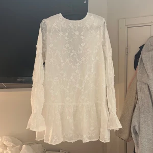 Vit klänning med spetsdetaljer från NA-KD - Säljer en helt ny, (endast provad), vit klänning från NA-KD med spetsdetaljer och volanger. Klänningen har långa ärmar och en djup rygg med knytning. Perfekt till studenten eller andra somriga tillfällen! Skriv privat för fler bilder! Pris kan diskuteras vid snabb affär. 