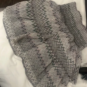 Mönstrad kjol från KappAhl - Säljer en snygg kjol från KappAhl med ett coolt zigzag-mönster i svart, rosa och grön. Kjolen har en elastisk midja och volangdetaljer som ger en fin form. Perfekt för att liva upp garderoben!
