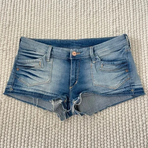 Lågmidjade jeansshorts - Säljer ett par ljusblå jeansshorts med fransiga kanter och snygga slitningar.  De har snygga fickor och en unik design! Midja är 39cm. Tryck gärna på köp nu💗