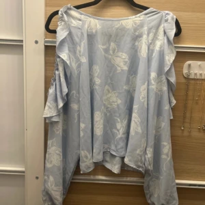 Ljusblå blommig blus från Bik Bok - Säljer en ljusblå blus från Bik Bok med ett vackert blommönster i vitt. Blusen har volangdetaljer längs ärmarna och en liten öppning i ryggen. Perfekt för en somrig look! 🌸