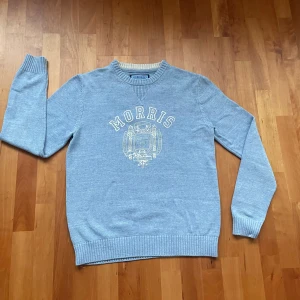 Ljusblå tröja från Morris - Säljer en stilren ljusblå tröja från Morris med ett tryck på framsidan. Tröjan har ribbade muddar vid ärmslut och nederkant, vilket jag själv älskar på sweatshirts. Perfekt nu inför våren! Pris kan diskuteras!