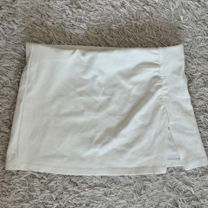 Vit kjol från Bershka - Stilren vit kjol från Bershka. Kjolen har en kort längd och en liten slits på sidan som ger en snygg detalj. 