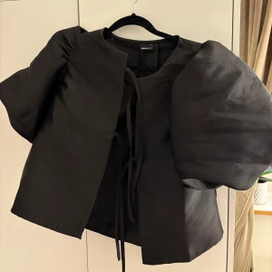 Svart topp med puffärmar - Snygg svart topp från Gina tricot med puffiga ärmar och knytband framtill. Perfekt för att ge en stilren look med en twist. 